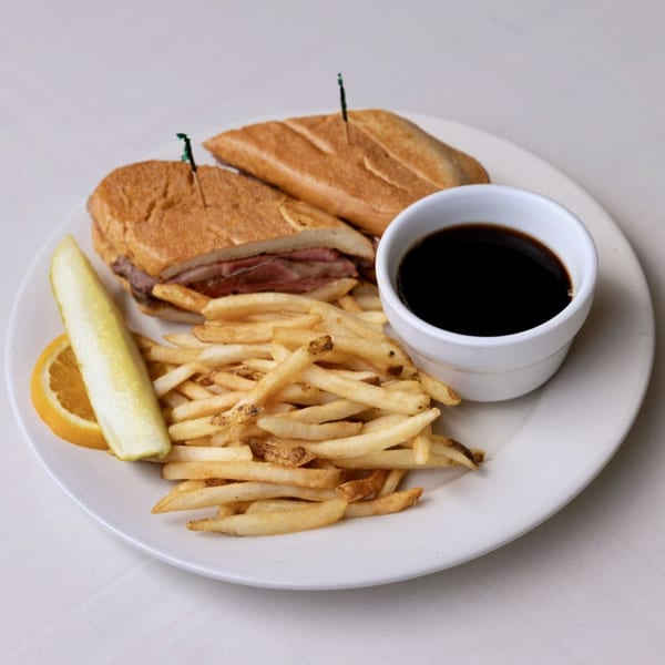 Effie's French dip sandwich with fries, a pickle spear, orange slice, and au jus.