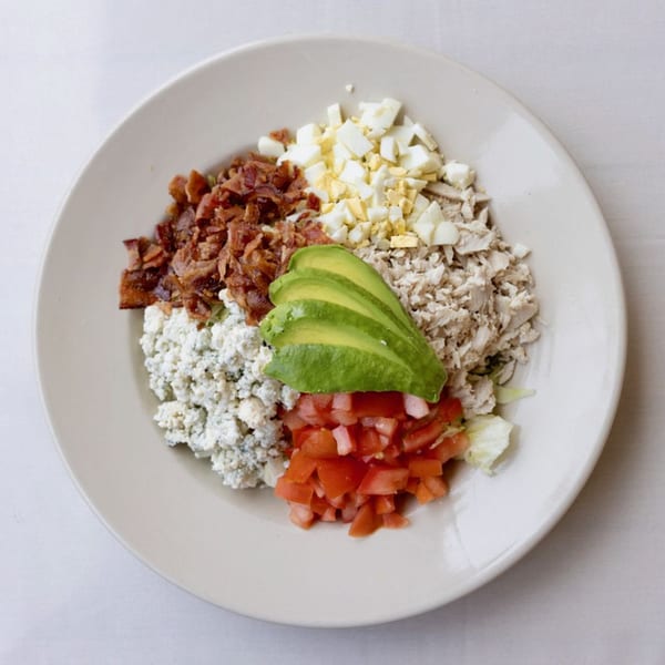 Overhead view of a Cobb salad with bacon, egg, chicken, avocado, blue cheese, and tomatoes.